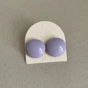 Close-up view of elegant purple round bean-shaped drop oil stud earrings on a cream card