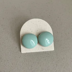 Detail of mint green enamel button earrings with a glossy finish on canvas board