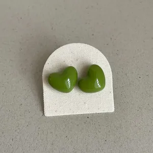 Macro view of bright green heart-shaped stud earrings with glossy enamel finish.