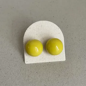 Detailed close-up view of vibrant yellow enamel bean-shaped stud earrings on a card