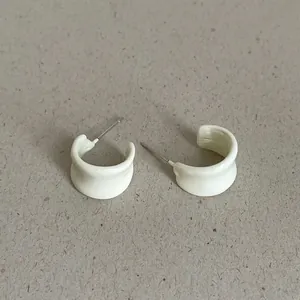 Detail view of off-white geometric bean-shaped hoop earrings on textured background