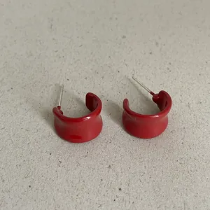 Close-up of red enamel bean-shaped geometric stud earrings on paper background, fashion style