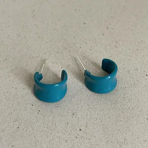 Close-up of teal drip oil C-shaped geometric hoop earrings on a textured background.