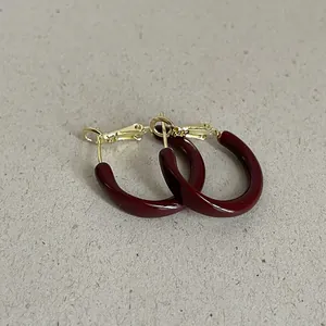 Close-up of dark red drip oil hoop earrings with elegant gold twisted metal details.