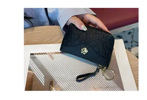 Gros plan d'un porte-monnaie en cuir noir gaufré avec fleur dorée et porte-clés.
