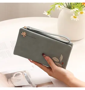 Detailed close-up of a stylish grey-green PU leather long wallet with leaf print in hand