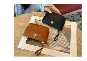 Détail d'un élégant mini porte-monnaie en cuir gaufré avec fleur dorée et porte-clés.