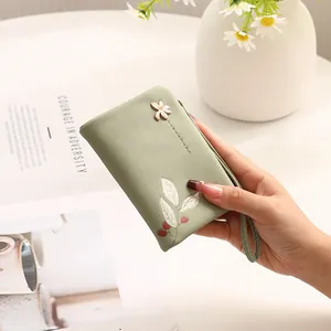 Close-up of a mint green floral wallet with wrist strap held by hand