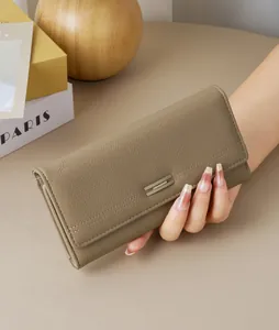 Detailed view of elegant taupe pebbled leather long wallet held in a woman's hand.