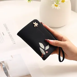 Close-up of black floral print short wallet with gold flower clasp and wrist strap
