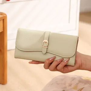 Macro detail of a cream pebble leather long wallet for women held by an elegant hand