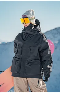 Modello con giacca da sci nera multitasche e snowboard in montagna tra le vette innevate