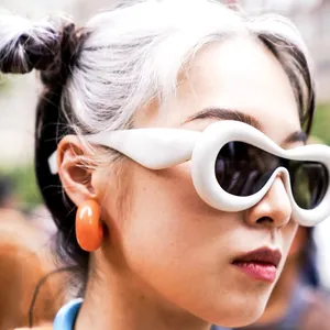 Detailed shot of avant-garde white oval sunglasses and chunky orange hoop earring