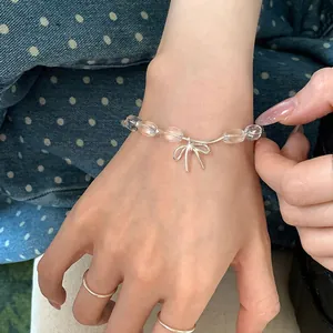 Dettaglio di un delicato bracciale di perle trasparenti con ciondolo a fiocco argento.