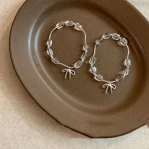Dettaglio del bracciale di perle trasparenti con un delicato ciondolo a fiocco argento.