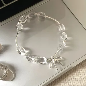 Dettaglio di un bracciale di perline trasparenti con ciondolo a fiocco argentato