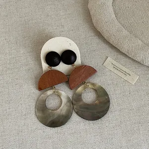 Macro detail of retro shell and wood patchwork drop earrings on textured linen background