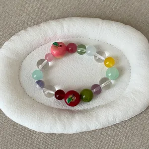 Kleurrijke kralenarmband met zoete appelbedeltjes op een witte getextureerde presentatieschaal