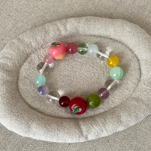 Detailopname van een kleurrijke kralenarmband met appelbedeltjes op een stoffen dienblad.