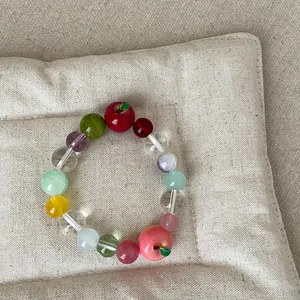 Detail van een kleurrijke kralenarmband met schattige appelbedeltjes op een beige stoffen basis.