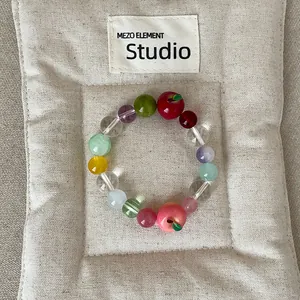 Detailweergave van kleurrijke kralenarmband met appelbedels op een beige stoffen pad