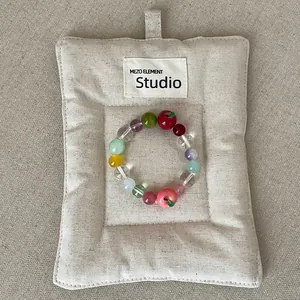 Kleurrijke kralen elastische armband met rode en roze appelbedels op een linnen kussen