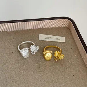 Detailed view of textured metal jar and flower open ring in gold and silver finish