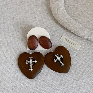Detail of vintage wooden heart earrings with silver-tone cross and clear gemstone adornment.