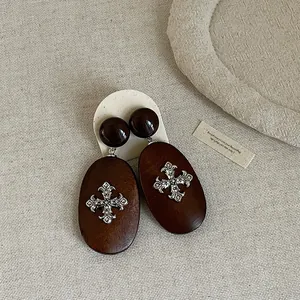 Detail view of retro dark brown wooden earrings with ornate silver cross emblem.