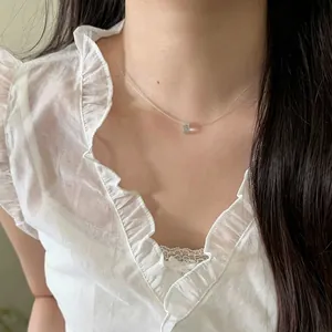 Close-up of minimalist invisible fishline necklace with a tiny blue teardrop pendant.