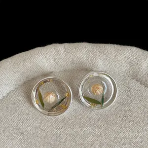 Detail macro view of transparent resin stud earrings with real dried flower and gold leaf.