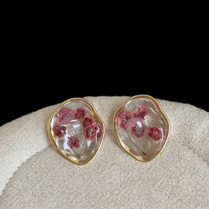 Detail view of vintage resin earrings with encapsulated dried pink flowers in gold frames