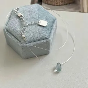Close-up of a minimalist blue teardrop pendant on a clear invisible fishing line cord.
