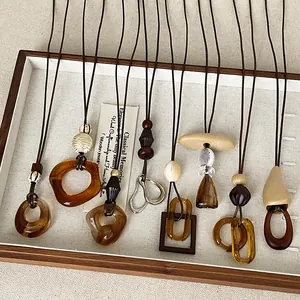 Detailed view of Maillard style amber resin necklaces with geometric pendants in a wooden tray
