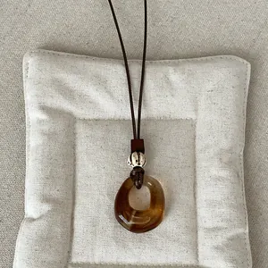 Close-up of vintage amber geometric resin pendant on a long brown cord necklace