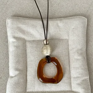 Close-up of amber geometric resin pendant necklace on beige cushion, vintage Maillard style.