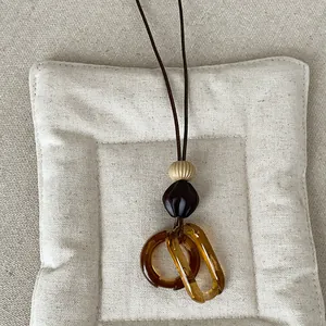 Close-up of amber resin geometric pendant on a minimalist long brown cord necklace