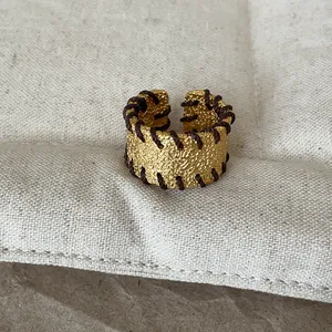 Nahaufnahme eines goldfarbenen strukturierten Rings mit brauner Fadenwicklung Details.