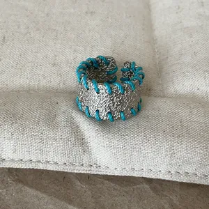 Detaillierte Makroansicht eines strukturierten Silberrings mit blauen Webfäden.