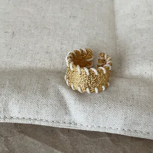 Detailansicht eines goldenen Metallrings mit Struktur und weißem geflochtenem Faden am Rand