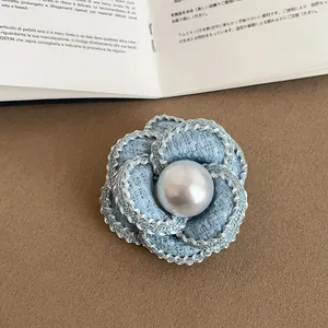 Detailed close-up of a light blue tweed camellia flower brooch with a glossy pearl center