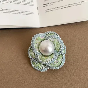 Macro shot of an elegant green tweed camellia flower brooch with a large central pearl