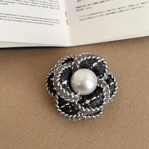 Close-up of elegant black tweed camellia brooch with central white pearl detail.