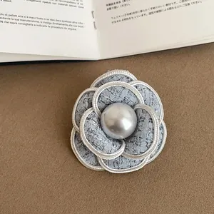 Elegant tweed camellia brooch with a central pearl, featuring a chic braided edge.