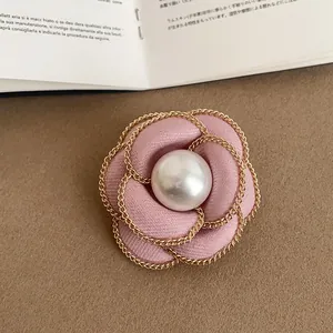 Macro close-up view of pink fabric camellia flower brooch with gold chain and pearl center