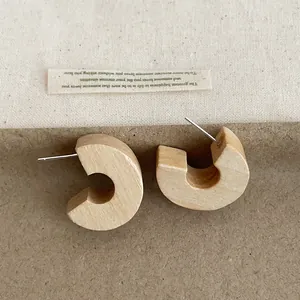 Macro view of chunky C-shaped wooden hoop earrings with natural wood grain texture