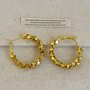 Gros plan de boucles d'oreilles créoles dorées texturées avec effet pailleté.