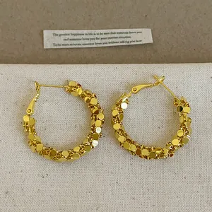 Gros plan de boucles d'oreilles créoles dorées avec un design à texture métallique étincelante