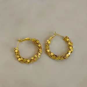 Gros plan de boucles d'oreilles créoles dorées avec texture facettée argent concassé.