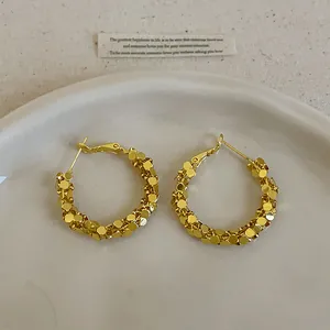Gros plan de boucles d'oreilles créoles dorées effet froissé sur un plateau blanc